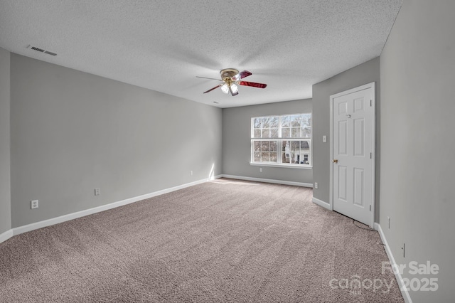 carpeted empty room with a textured ceiling, baseboards, a ceiling fan, and visible vents