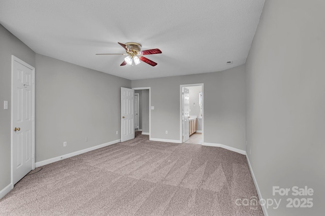 unfurnished bedroom with light carpet, baseboards, a textured ceiling, ensuite bath, and a ceiling fan