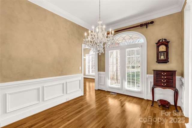 unfurnished dining area featuring wood-type flooring, ornamental molding, and a notable chandelier