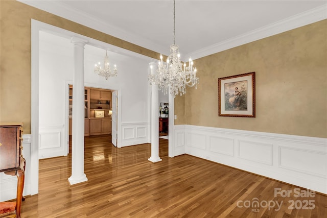 unfurnished dining area with wood-type flooring, decorative columns, and an inviting chandelier