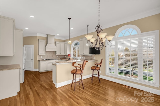 kitchen featuring decorative backsplash, a kitchen breakfast bar, premium range hood, decorative light fixtures, and white cabinetry