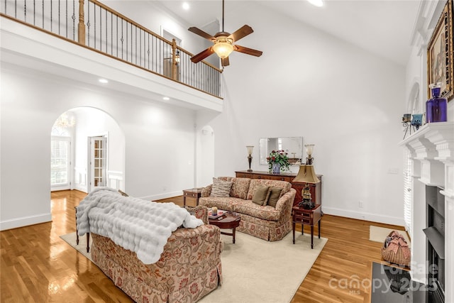 living room with ceiling fan, a towering ceiling, and light hardwood / wood-style flooring