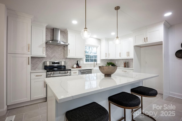 kitchen with appliances with stainless steel finishes, a kitchen island, wall chimney exhaust hood, and pendant lighting