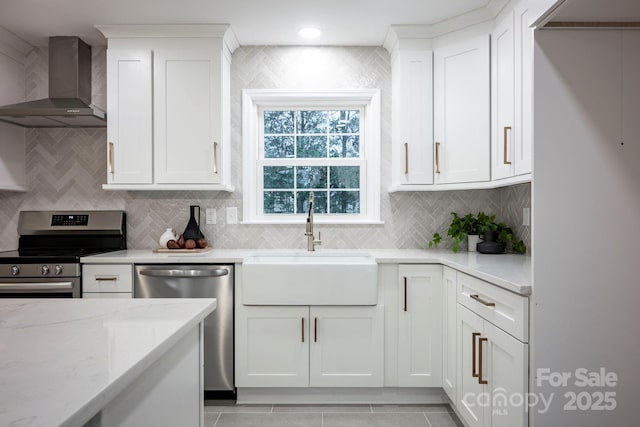 kitchen with sink, light stone counters, wall chimney range hood, stainless steel appliances, and white cabinets