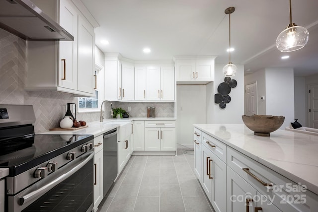 kitchen featuring appliances with stainless steel finishes, decorative light fixtures, wall chimney range hood, white cabinets, and light stone countertops