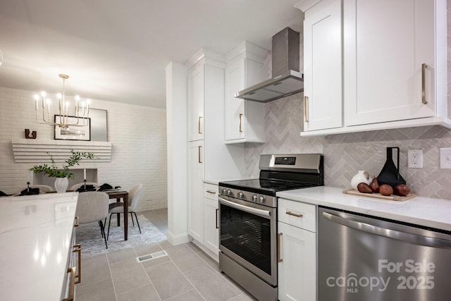 kitchen with appliances with stainless steel finishes, wall chimney exhaust hood, light stone countertops, pendant lighting, and white cabinetry