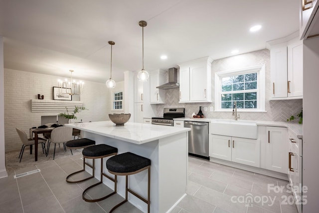 kitchen with appliances with stainless steel finishes, wall chimney exhaust hood, pendant lighting, a center island, and white cabinetry