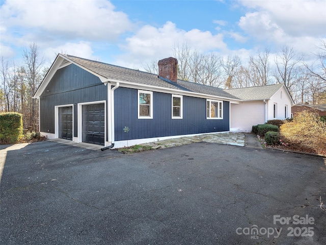 exterior space featuring a garage, roof with shingles, and a chimney