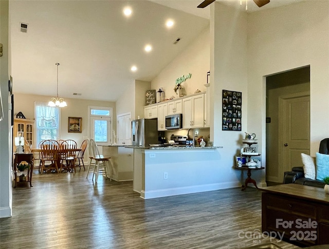 kitchen with kitchen peninsula, appliances with stainless steel finishes, a kitchen breakfast bar, high vaulted ceiling, and white cabinets