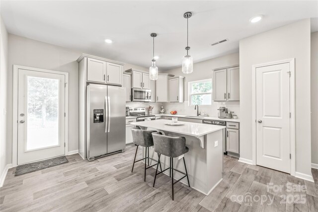 kitchen featuring sink, appliances with stainless steel finishes, decorative light fixtures, a kitchen island, and a breakfast bar area