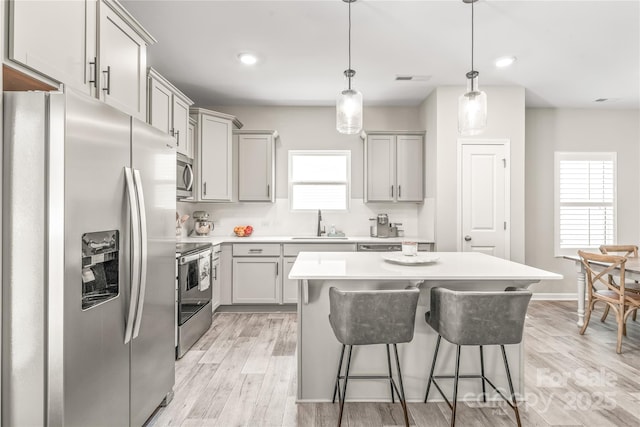 kitchen featuring decorative light fixtures, a center island, light wood-type flooring, and appliances with stainless steel finishes