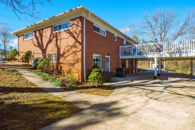 view of property exterior featuring central AC unit, driveway, a carport, a deck, and brick siding