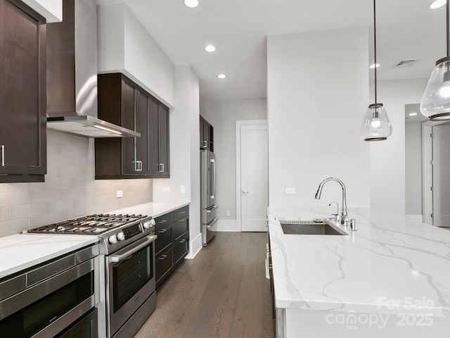 kitchen featuring sink, hanging light fixtures, wall chimney exhaust hood, light stone counters, and stainless steel appliances