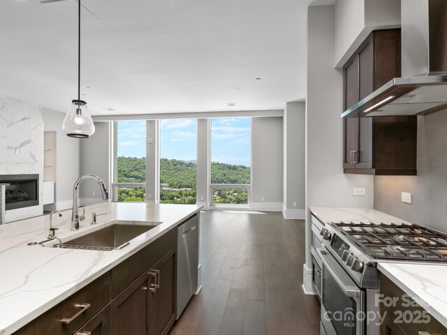 kitchen featuring backsplash, wall chimney range hood, sink, decorative light fixtures, and stainless steel appliances