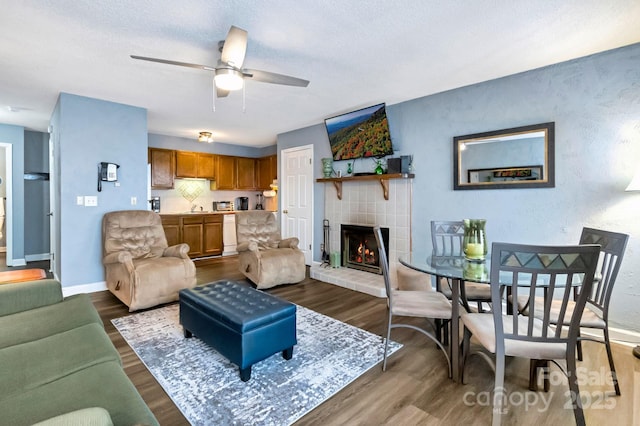 living room with a textured ceiling, ceiling fan, a fireplace, and dark wood-type flooring