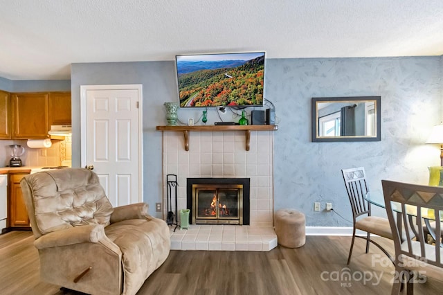 living room featuring a tiled fireplace, light hardwood / wood-style flooring, and a textured ceiling