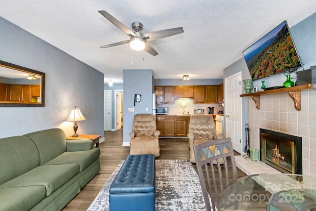 living room with a fireplace, a textured ceiling, light hardwood / wood-style floors, and ceiling fan