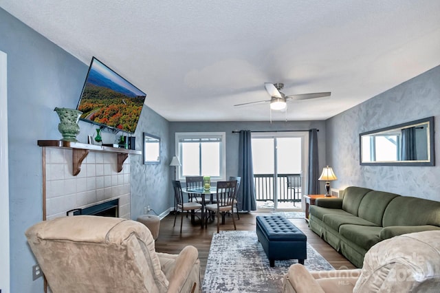 living room with a textured ceiling, ceiling fan, dark wood-type flooring, and a tiled fireplace