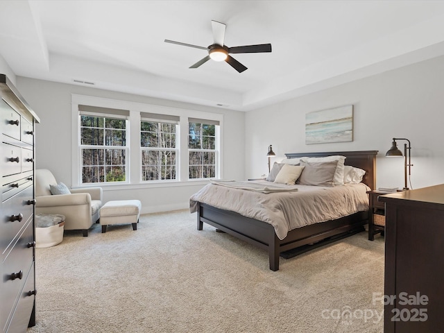 bedroom with ceiling fan, light carpet, and a tray ceiling