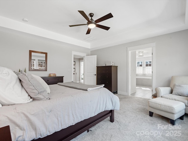 bedroom featuring light carpet, a raised ceiling, ensuite bath, and ceiling fan