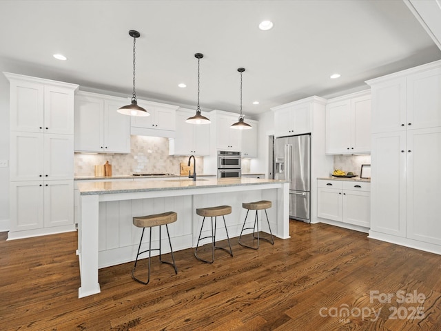 kitchen featuring appliances with stainless steel finishes, decorative light fixtures, white cabinets, dark hardwood / wood-style floors, and an island with sink