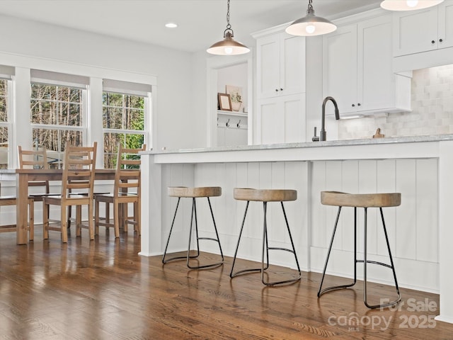 kitchen with a kitchen bar, light stone countertops, backsplash, decorative light fixtures, and white cabinetry