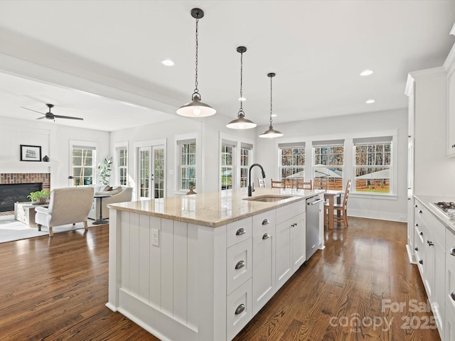 kitchen featuring sink, a fireplace, white cabinets, a center island with sink, and appliances with stainless steel finishes