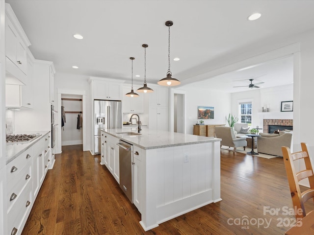 kitchen featuring white cabinetry, sink, stainless steel appliances, decorative light fixtures, and a center island with sink