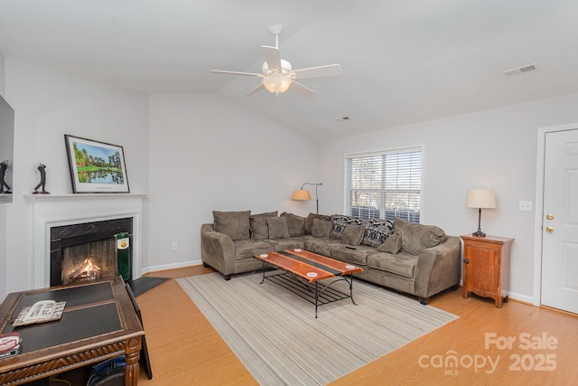 living room with vaulted ceiling, ceiling fan, a high end fireplace, and light hardwood / wood-style flooring