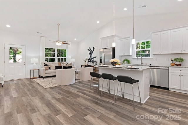 kitchen with ceiling fan, light stone countertops, appliances with stainless steel finishes, decorative light fixtures, and white cabinetry