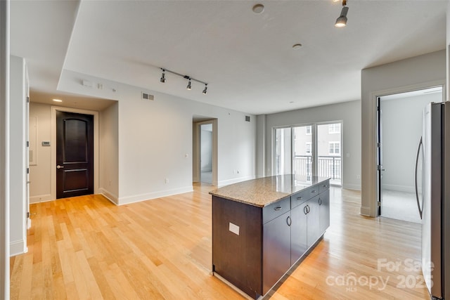 kitchen with rail lighting, stainless steel fridge, a center island, dark brown cabinetry, and light wood-type flooring