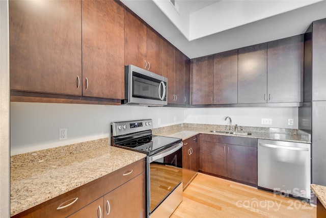 kitchen featuring dark brown cabinetry, sink, light stone counters, stainless steel appliances, and light hardwood / wood-style floors