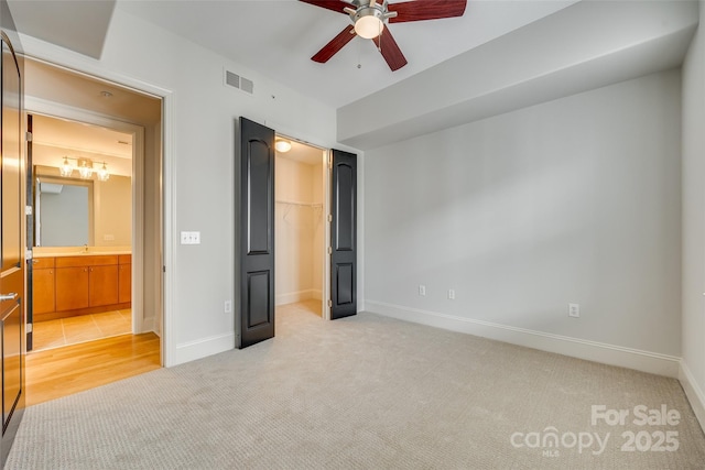 unfurnished bedroom featuring sink, a spacious closet, light colored carpet, a closet, and ceiling fan