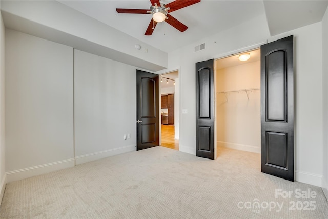 unfurnished bedroom with a spacious closet, light carpet, ceiling fan, and a closet