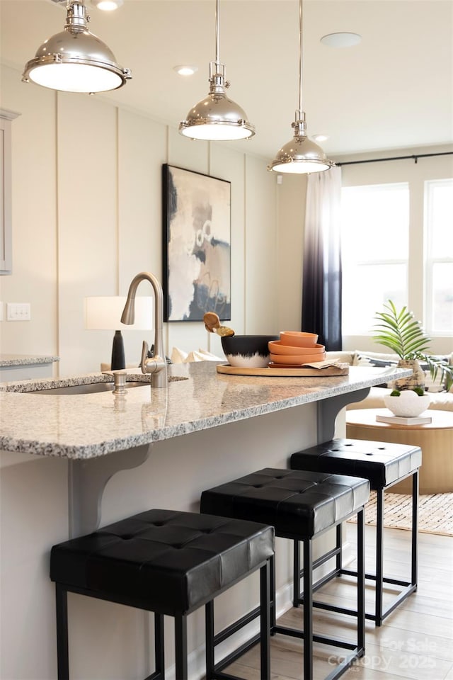 kitchen with light stone countertops, light hardwood / wood-style floors, hanging light fixtures, and sink