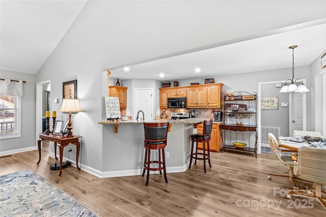 kitchen with light stone counters, tasteful backsplash, vaulted ceiling, light wood-type flooring, and a kitchen breakfast bar