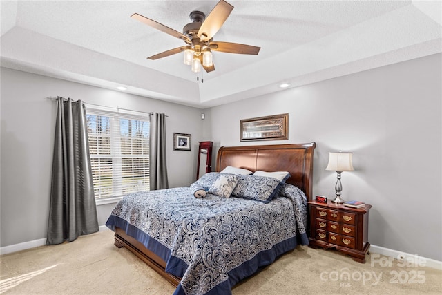 carpeted bedroom with ceiling fan and a tray ceiling