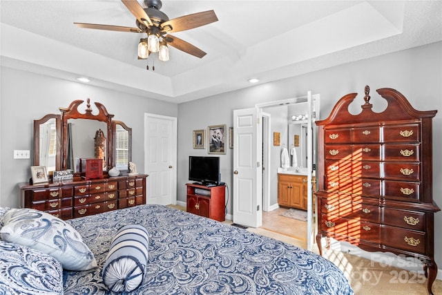 bedroom with a tray ceiling, ensuite bath, and ceiling fan