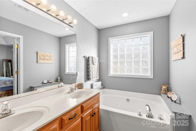 bathroom with plenty of natural light, vanity, a textured ceiling, and a tub