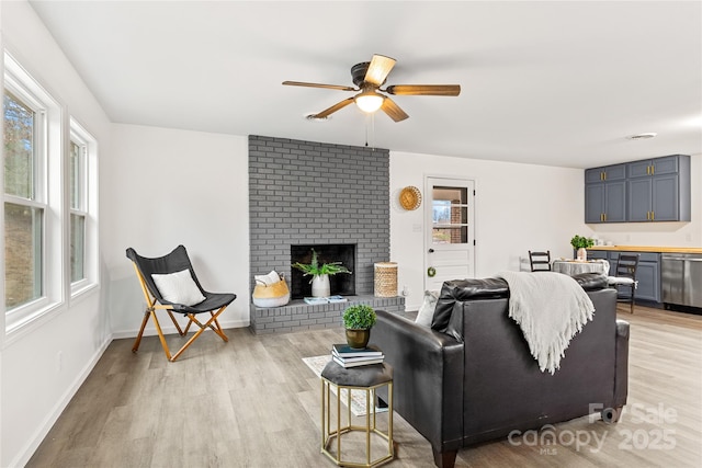 living room featuring light wood-type flooring, a brick fireplace, ceiling fan, and a healthy amount of sunlight