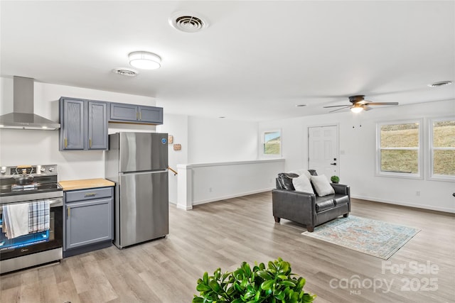 kitchen featuring gray cabinetry, ceiling fan, wall chimney exhaust hood, stainless steel appliances, and light hardwood / wood-style flooring