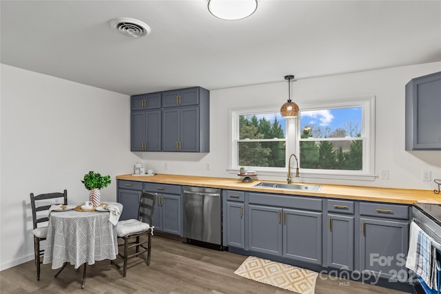 kitchen with butcher block counters, sink, stainless steel dishwasher, and decorative light fixtures