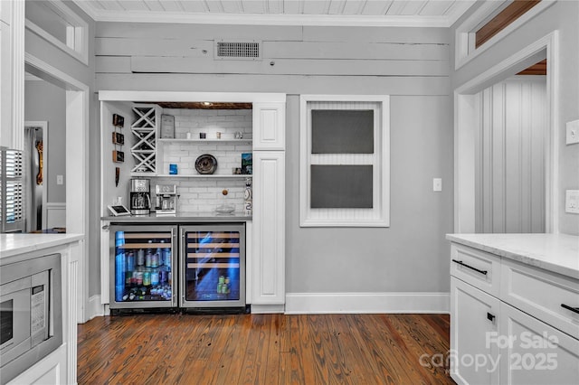 bar with wine cooler, white cabinetry, stainless steel microwave, and wooden walls