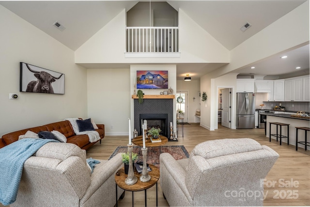 living room featuring high vaulted ceiling, a fireplace, and light hardwood / wood-style floors