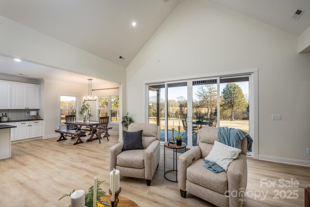 living room featuring a notable chandelier, high vaulted ceiling, and light wood-type flooring