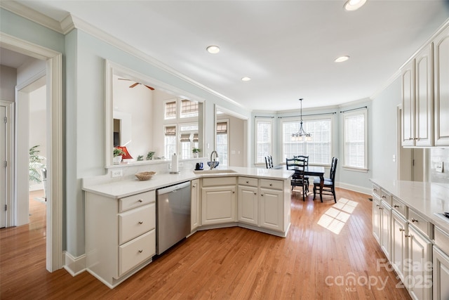 kitchen with decorative light fixtures, dishwasher, sink, ornamental molding, and light hardwood / wood-style floors