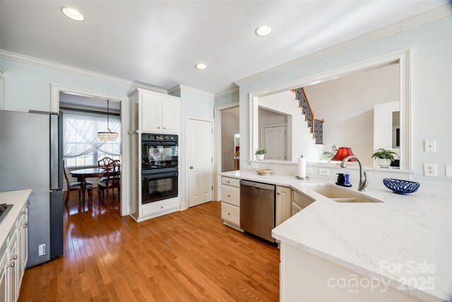 kitchen featuring sink, white cabinetry, stainless steel appliances, ornamental molding, and light wood-type flooring