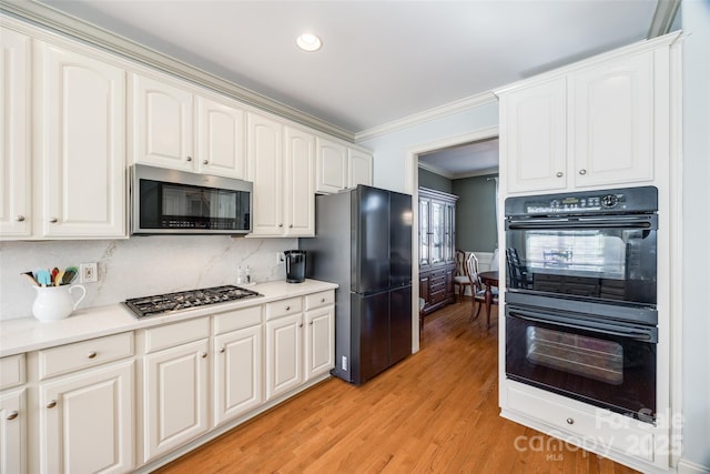 kitchen with crown molding, light hardwood / wood-style flooring, white cabinetry, tasteful backsplash, and black appliances