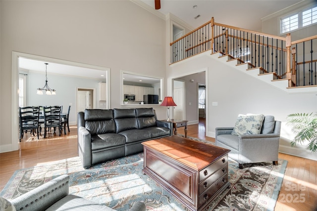 living room featuring a high ceiling, ornamental molding, a chandelier, and light wood-type flooring