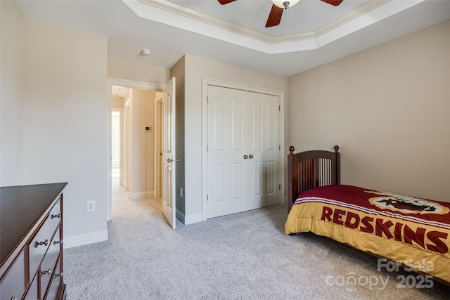 bedroom with ceiling fan, a tray ceiling, ornamental molding, light colored carpet, and a closet